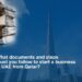 A stack of organized documents and binders on the left side of the image symbolizes the paperwork required. The iconic Burj Khalifa in Dubai is prominently displayed on the right, against a clear blue sky. The text overlay reads, "What documents and steps must you follow to start a business in UAE from Qatar?" This image targets entrepreneurs and business professionals in Qatar looking to expand their operations to the UAE.